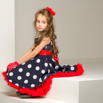 Beautiful Girl Wearing Polka Dot Dress and Black Shoes Sitting on White Stairs and Smiling at Camera, Full Length Portrait of Charming Coquettish Girl Posing in Retro Fashion Dress in Studio