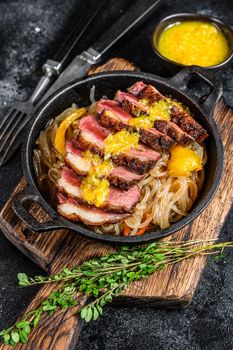 Grilled duck meat breast fillet steak with noodles and tangerines sauce. Black background. Top view.
