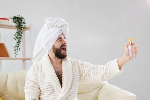 Bearded male with bath towel on his head applying spray water treatment on face. Spa, body and skin care for man concept