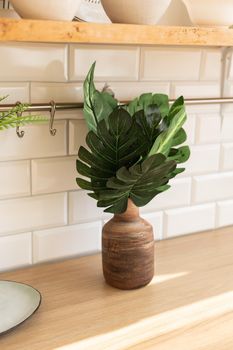 Artificial monstera leaves on a vase in scandinavian kitchen style background.