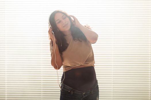 Portrait of pregnant woman sitting on sofa at home and listening music in headphones.