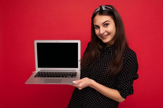 Photo of beautiful smiling brunet girl wearing black clothes holding computer laptop looking at camera isolated on colourful wall background. Empty space