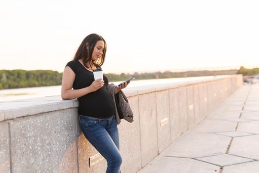 Close-up of pregnant woman with smartphone at park. Pregnancy, technology and communication