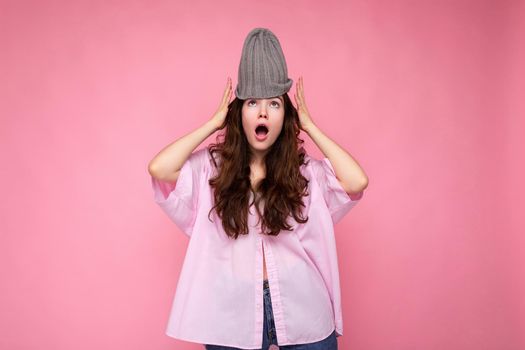 Attractive shocked amazed young brunette woman standing isolated over colorful background wall wearing everyday stylish outfit showing facial emotions looking at camera.