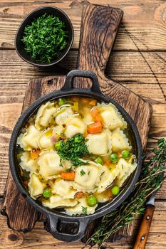 Broth soup with ravioli dumplings pasta in a pan. Wooden background. Top view.