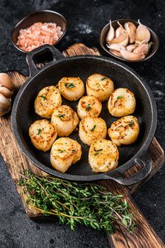 Fried scallops with butter sauce in a pan. Black background. Top view.