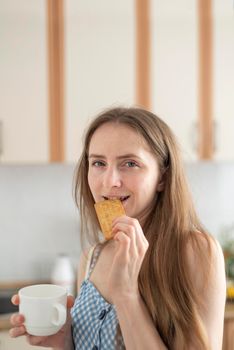 Young woman bites cracker and slyly looks at camera. Girl drinks coffee and eating cookies. Cheat meal. Vertical frame.