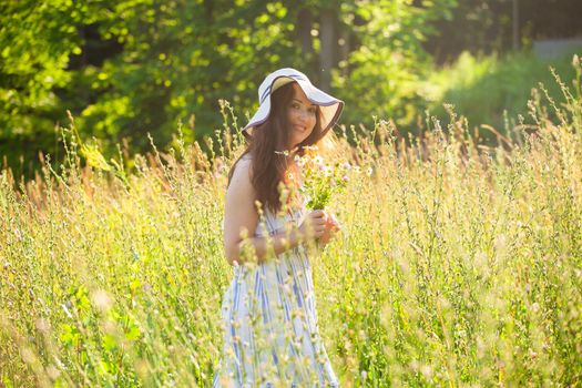 Rear view of beautiful young woman walking among wildflowers on sunny summer day. Joy of communicating with summer nature