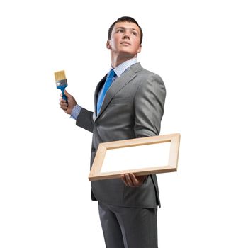 Creative businessman painter holding paint brush and whiteboard in hands. Portrait of handsome young man in business suit and tie isolated on white background. Inspiration and creativity in business.
