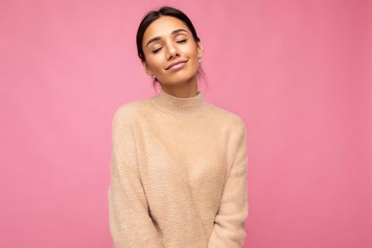 Photo of young beautiful happy cute brunette woman wearing beige jersey . Sexy carefree female person posing isolated near pink wall in studio with free space. Positive model with natural makeup.