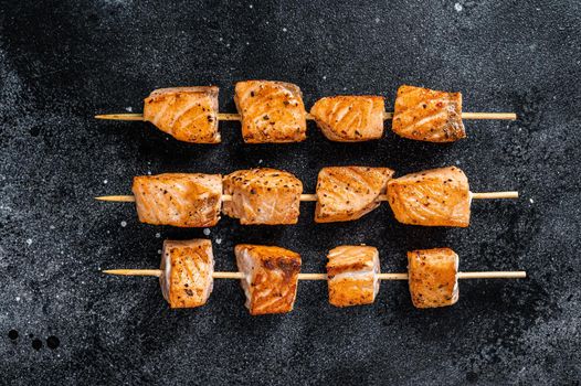 Grilled salmon kebab skewers. Black background. Top View.