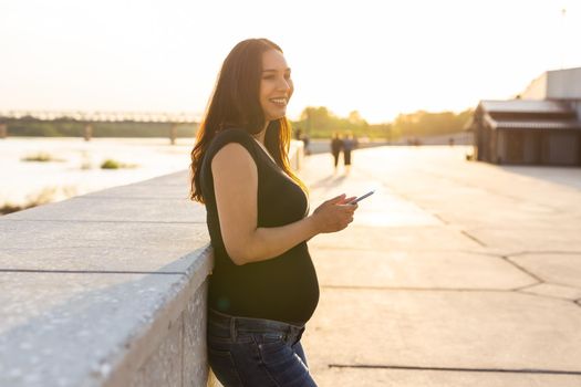 Pregnant woman with smartphone outdoors. Pregnancy, technology and communication.