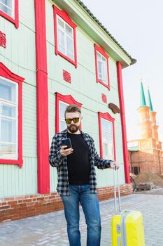 Full body side portrait of happy travel man with suitcase walking along the building in city