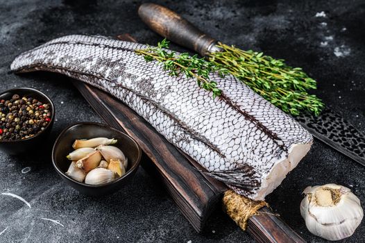 Raw grenadier macrurus white fish on a wooden cutting board. Black background. Top view.