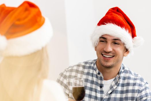 Young couple in Santa hats drinking wine and celebrating Christmas, close up