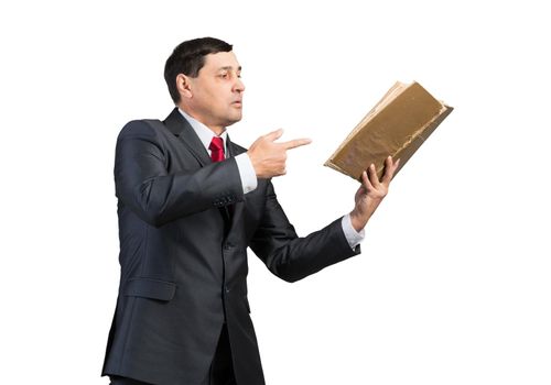 Senior businessman finger pointing into open book. Portrait of adult man in business suit and tie standing on white background. Manager holding big handbook. Professional reference information.