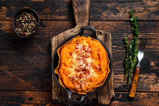 Baked in skin sweet potato batata stuffed with cheese and bacon. Dark Wooden background. Top view.