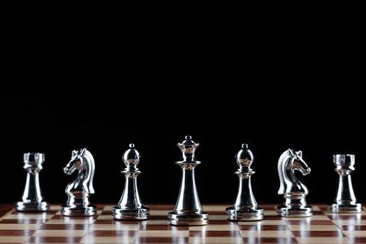 Silvery chess figures standing on chessboard. Intellectual competition and fight in business. Strategy planning and leadership concept with copy space. Silver chess pieces in row on black background.
