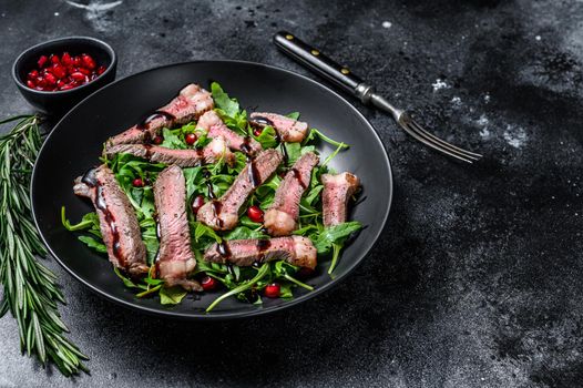 Grilled Beef Steak salad with arugula, pomegranate and greens vegetables. Black background. Top view. Copy space.