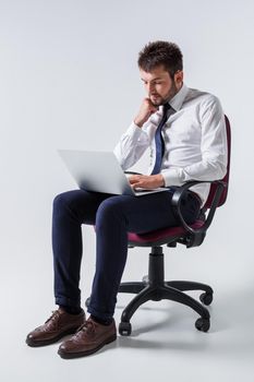 emotional young guy in office clothes working on a laptop computer and sitting on a chair