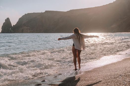 Selective focus. Happy carefree sensual woman with long hair in black swimwear posing at sunset beach. Silhouette of young beautiful playful positive woman outdoor. Summer vacation and trip concept.