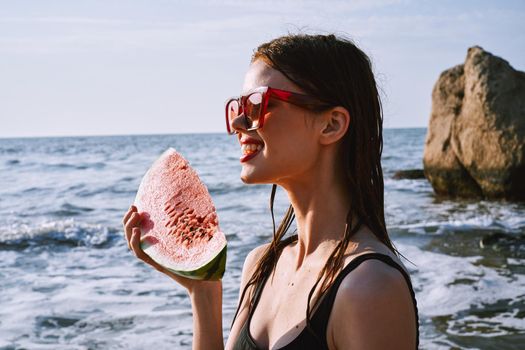 cheerful woman in black swimsuit eating watermelon on the beach. High quality photo