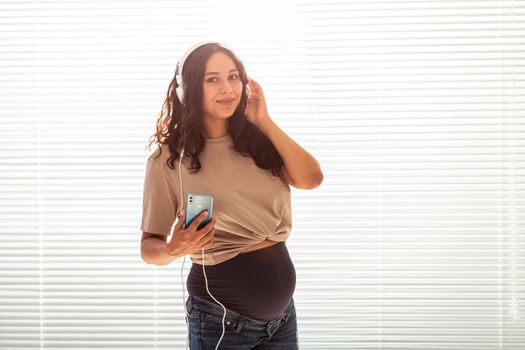 Portrait of pregnant woman sitting on sofa at home and listening music in headphones.