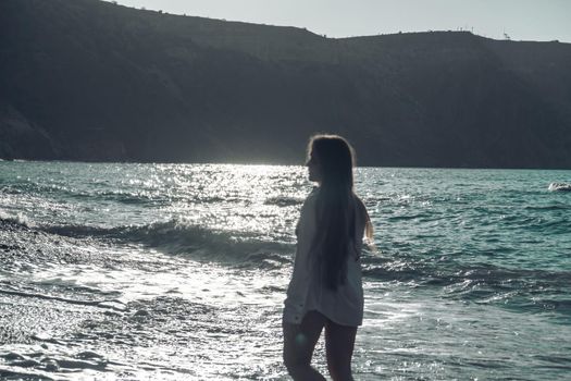 Selective focus. Happy carefree sensual woman with long hair in black swimwear posing at sunset beach. Silhouette of young beautiful playful positive woman outdoor. Summer vacation and trip concept.