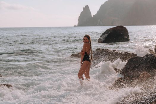 Selective focus. Happy carefree sensual woman with long hair in black swimwear posing at sunset beach. Silhouette of young beautiful playful positive woman outdoor. Summer vacation and trip concept.