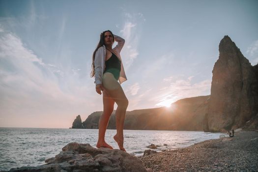 Selective focus. Happy carefree sensual woman with long hair in black swimwear posing at sunset beach. Silhouette of young beautiful playful positive woman outdoor. Summer vacation and trip concept.
