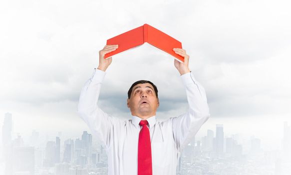 Senior businessman holding open diary overhead as roof. Man in white shirt and tie standing on cloudy cityscape background. Education and professional knowledges. Time management and day planning.