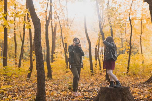 Child girl photographer takes pictures of a mother in the park in autumn. Hobbies, photo art and leisure concept