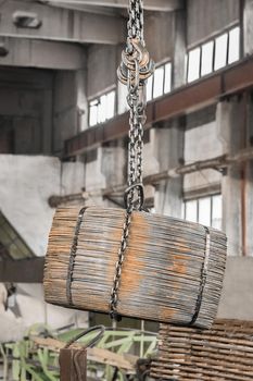 An overhead crane hoist with a hook and chain transports reinforced iron structures in the workshop of an industrial enterprise.