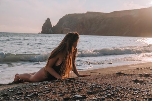 Selective focus. Happy carefree sensual woman with long hair in black swimwear posing at sunset beach. Silhouette of young beautiful playful positive woman outdoor. Summer vacation and trip concept.