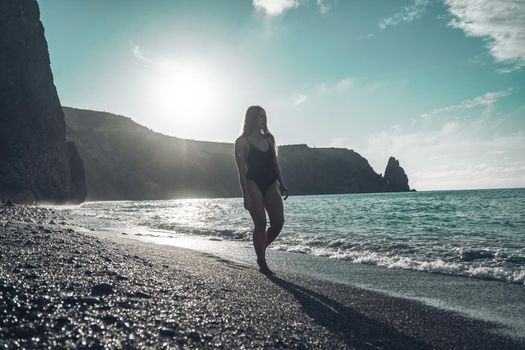 Selective focus. Happy carefree sensual woman with long hair in black swimwear posing at sunset beach. Silhouette of young beautiful playful positive woman outdoor. Summer vacation and trip concept.