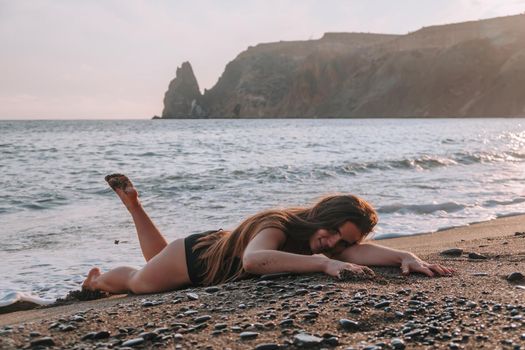 Selective focus. Happy carefree sensual woman with long hair in black swimwear posing at sunset beach. Silhouette of young beautiful playful positive woman outdoor. Summer vacation and trip concept.