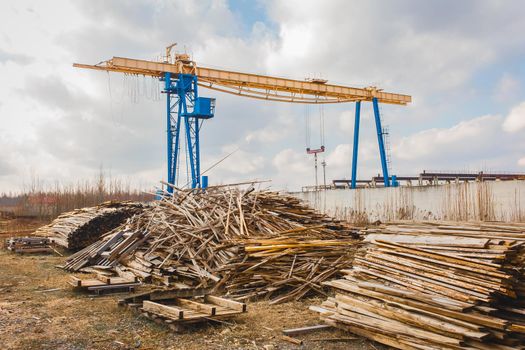 Industrial zone, construction site with piles of wooden waste and overhead hoist building crane.