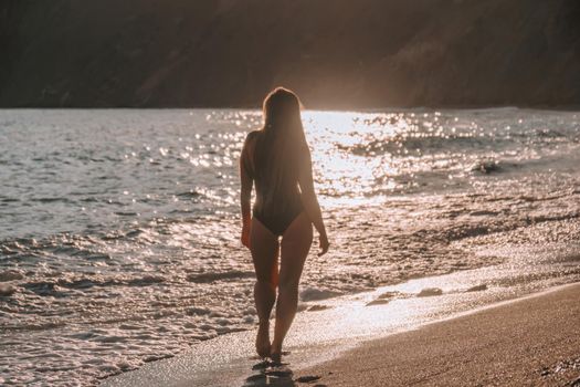 Selective focus. Happy carefree sensual woman with long hair in black swimwear posing at sunset beach. Silhouette of young beautiful playful positive woman outdoor. Summer vacation and trip concept.