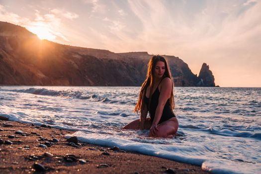 Selective focus. Happy carefree sensual woman with long hair in black swimwear posing at sunset beach. Silhouette of young beautiful playful positive woman outdoor. Summer vacation and trip concept.