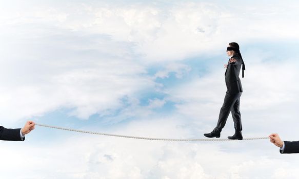 Businessman with blindfolder on eyes walking on rope over sky background