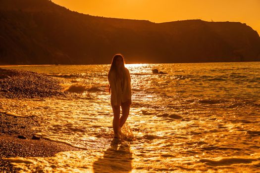 Selective focus. Happy carefree sensual woman with long hair in black swimwear posing at sunset beach. Silhouette of young beautiful playful positive woman outdoor. Summer vacation and trip concept.