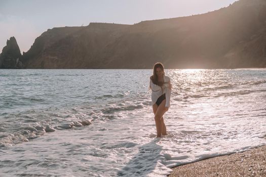 Selective focus. Happy carefree sensual woman with long hair in black swimwear posing at sunset beach. Silhouette of young beautiful playful positive woman outdoor. Summer vacation and trip concept.