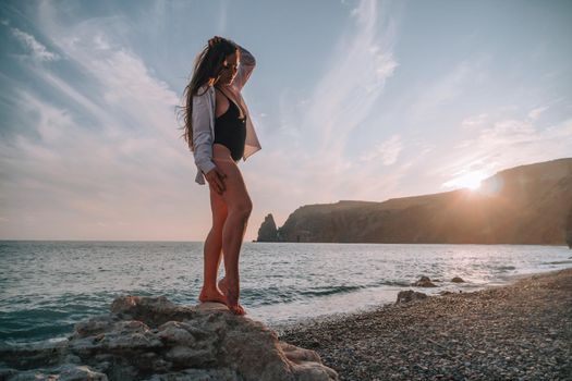 Selective focus. Happy carefree sensual woman with long hair in black swimwear posing at sunset beach. Silhouette of young beautiful playful positive woman outdoor. Summer vacation and trip concept.