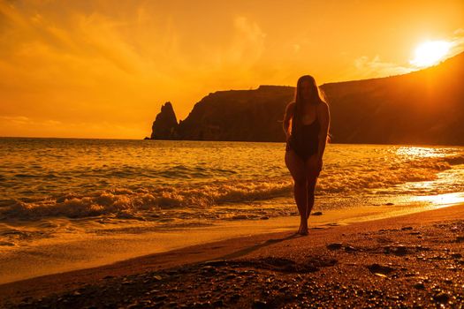 Selective focus. Happy carefree sensual woman with long hair in black swimwear posing at sunset beach. Silhouette of young beautiful playful positive woman outdoor. Summer vacation and trip concept.