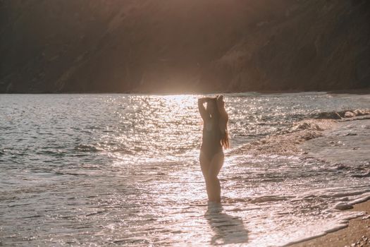 Selective focus. Happy carefree sensual woman with long hair in black swimwear posing at sunset beach. Silhouette of young beautiful playful positive woman outdoor. Summer vacation and trip concept.