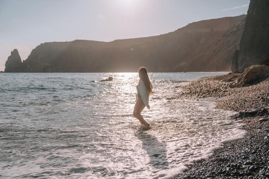 Selective focus. Happy carefree sensual woman with long hair in black swimwear posing at sunset beach. Silhouette of young beautiful playful positive woman outdoor. Summer vacation and trip concept.