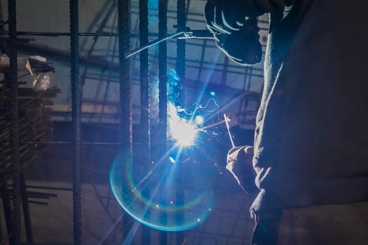 Working man is doing welding work on metal structures in a factory or industrial enterprise.