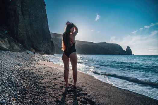 Selective focus. Happy carefree sensual woman with long hair in black swimwear posing at sunset beach. Silhouette of young beautiful playful positive woman outdoor. Summer vacation and trip concept.