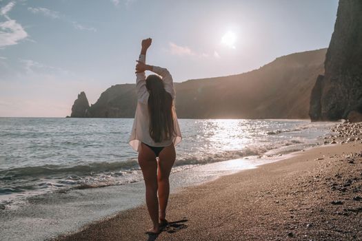 Selective focus. Happy carefree sensual woman with long hair in black swimwear posing at sunset beach. Silhouette of young beautiful playful positive woman outdoor. Summer vacation and trip concept.