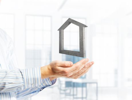 Cropped image of businessman in suit keeping stone house symbol in hands. Mixed media